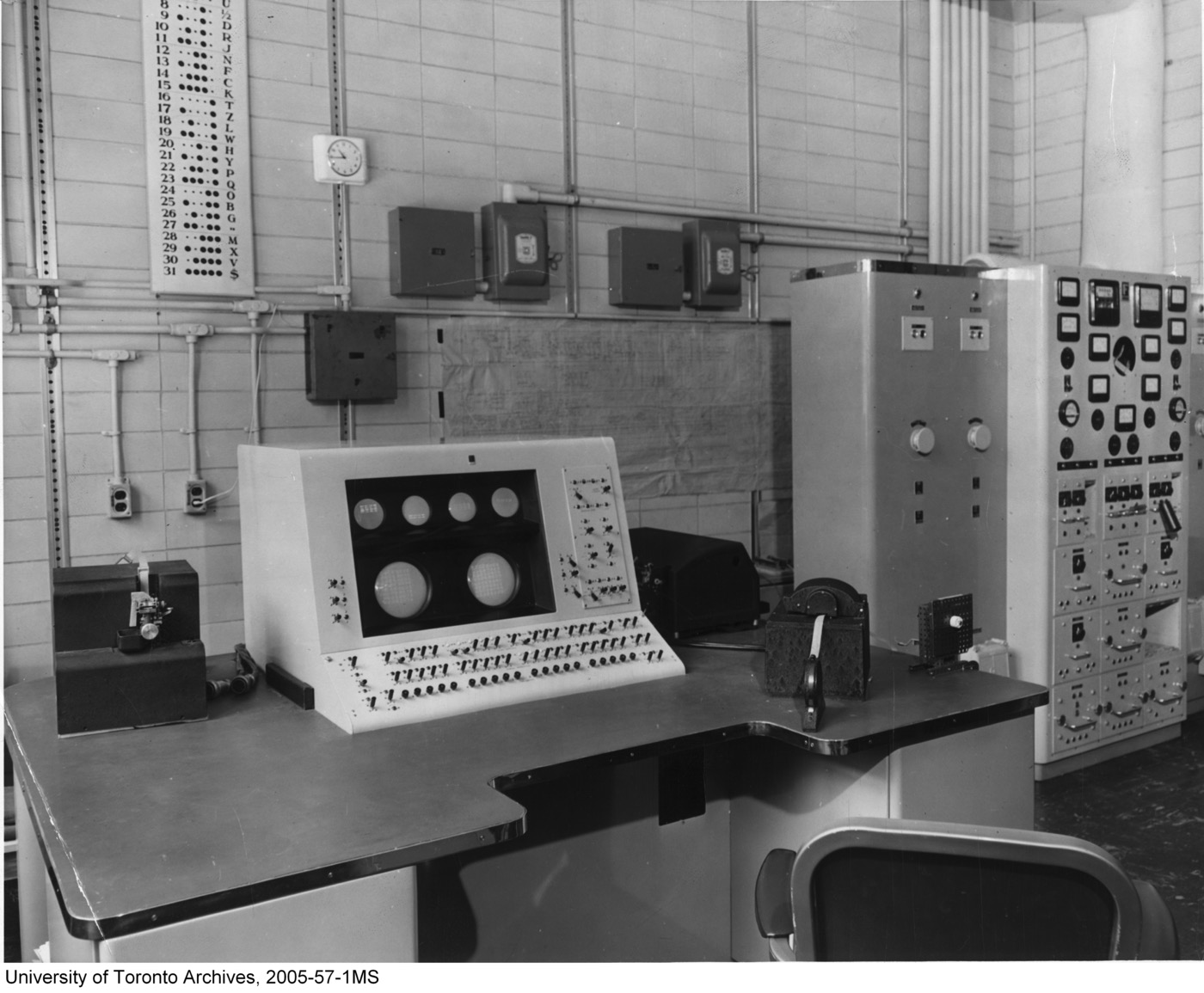 The console of the FERUT computer, a desk of dials and switches before tall equipment cabinets, around 1958